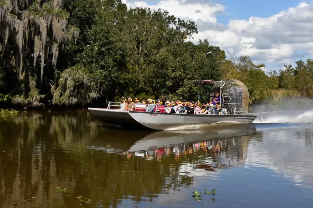 Large airboat full of riders cruising a bayou lined with Spanish moss
