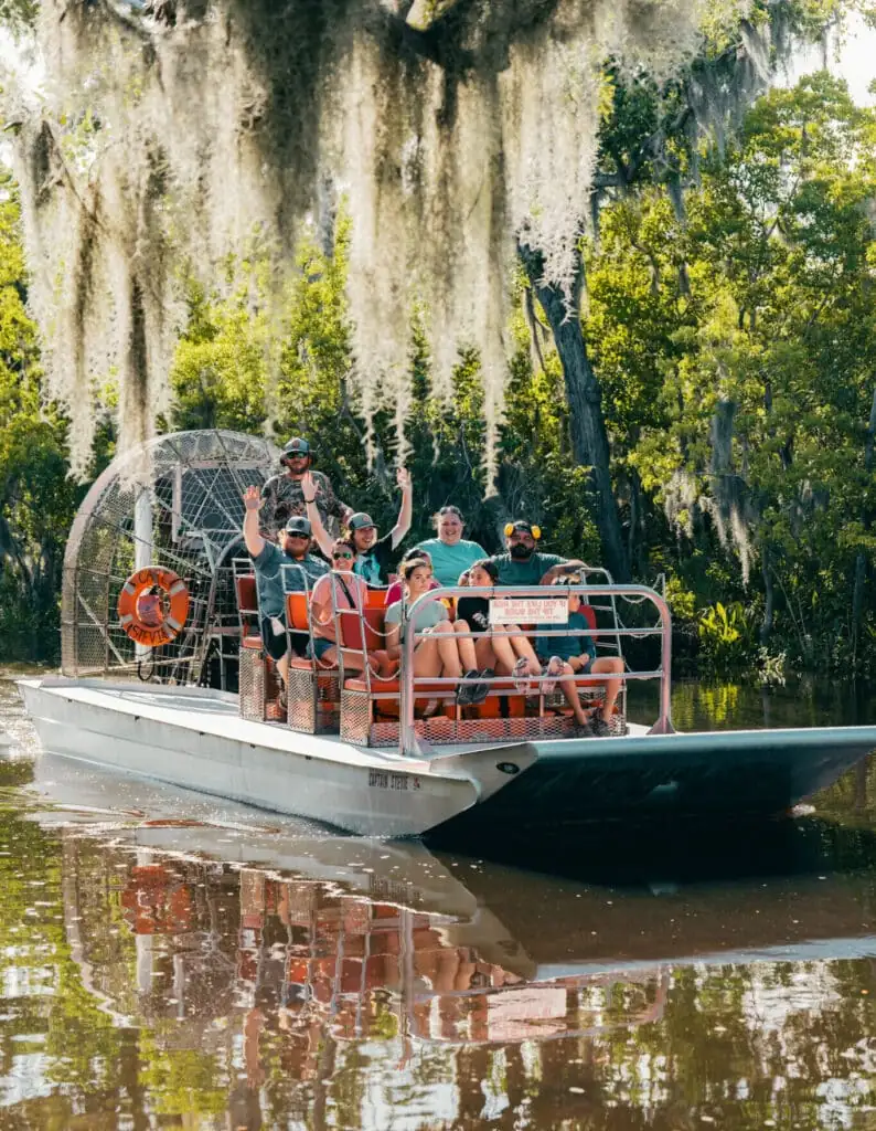 Riders throwing their hands up on an airboat under curtains of Spanish moss