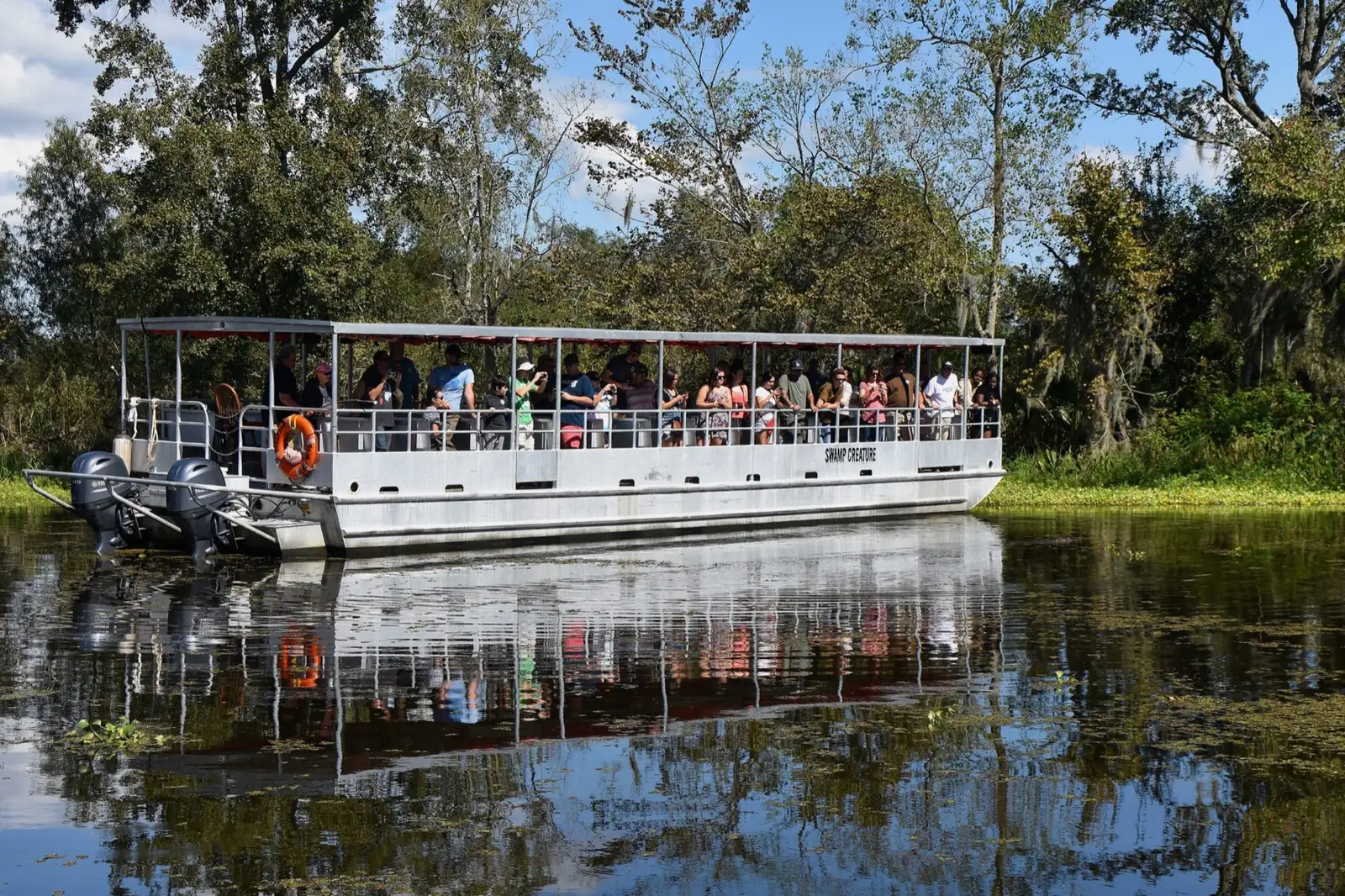 Covered pontoon boat full of passengers reflected in still swamp water