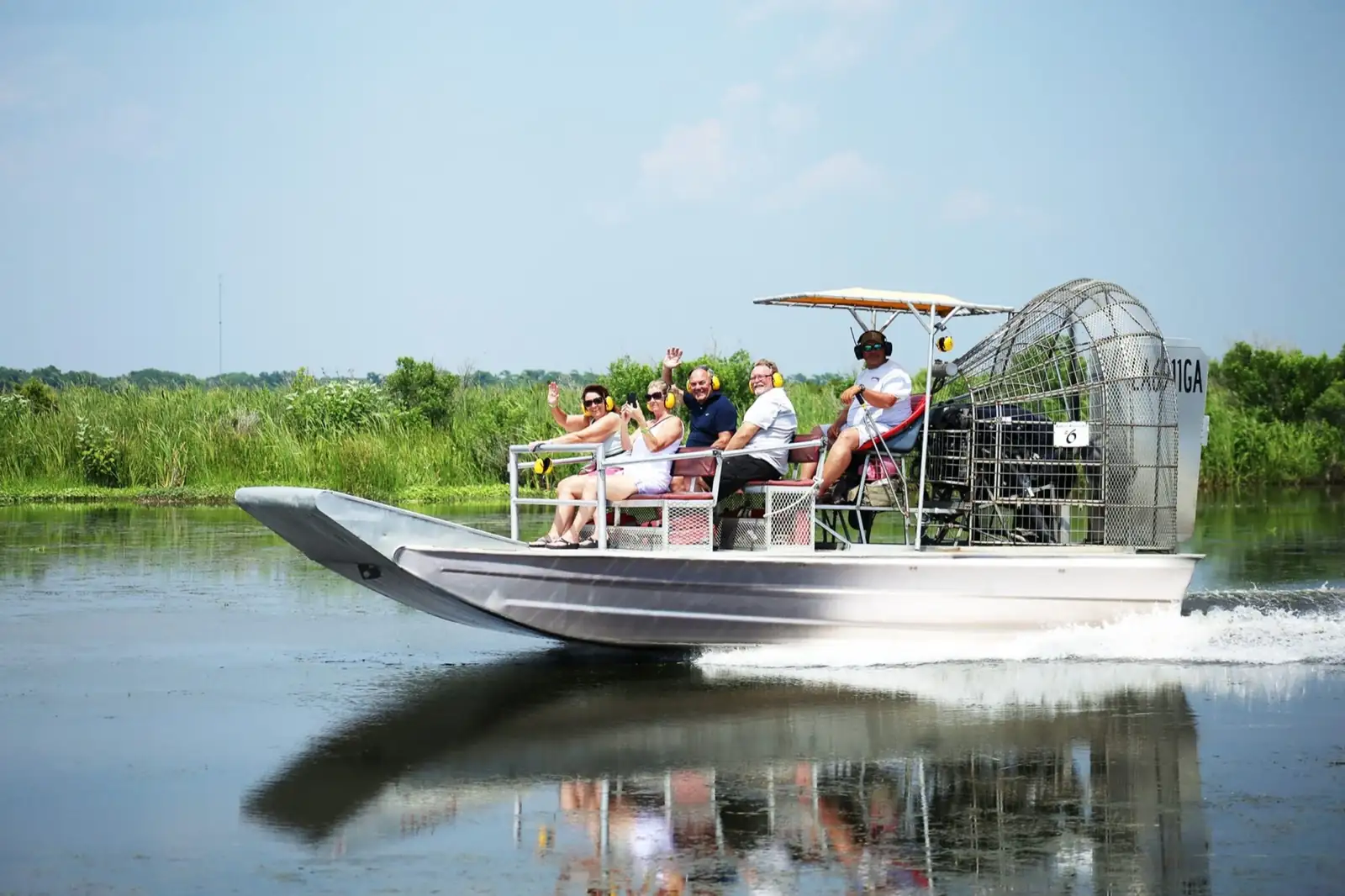 Small group waving from a silver airboat skimming across open marsh